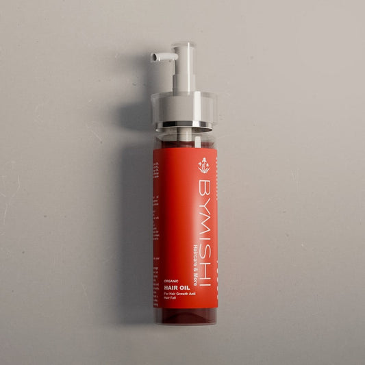 Red bottle of BYMISHI hair oil on a gray background
